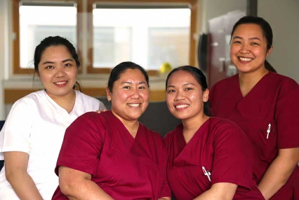Vier internationale Pflegefachkräfte lächeln gemeinsam in einem Klinikzimmer.